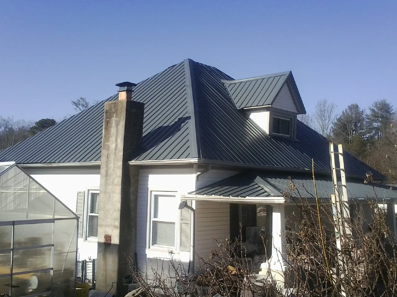 Dark blue standing seam metal roof on a white farmhouse with dormer — Slate & Tile Roof Repair by Roofing Brothers in New Florence