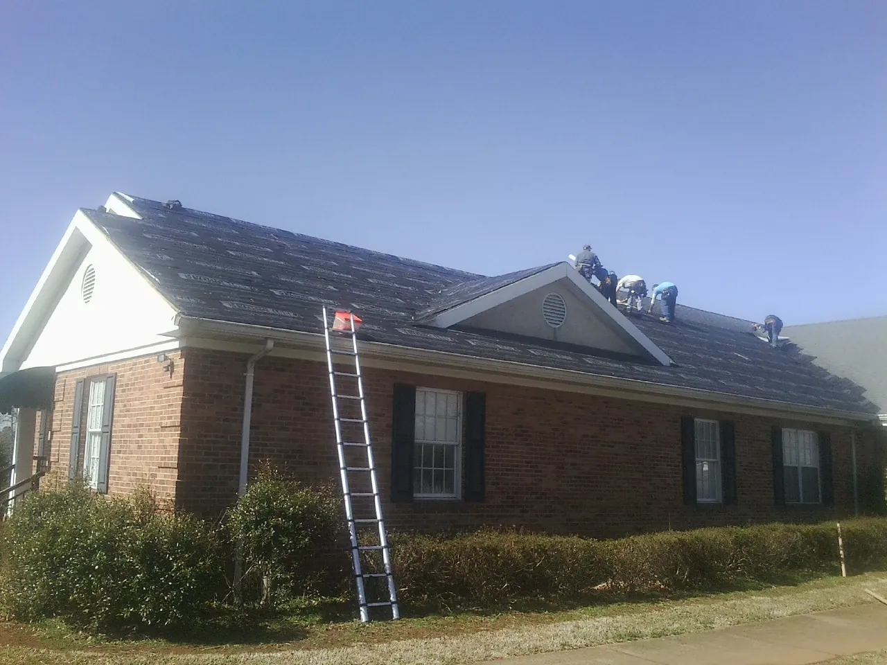 Crew tearing shingles off a brick ranch roof with a ladder set — Emergency Roof Repair work by our crew in New Florence