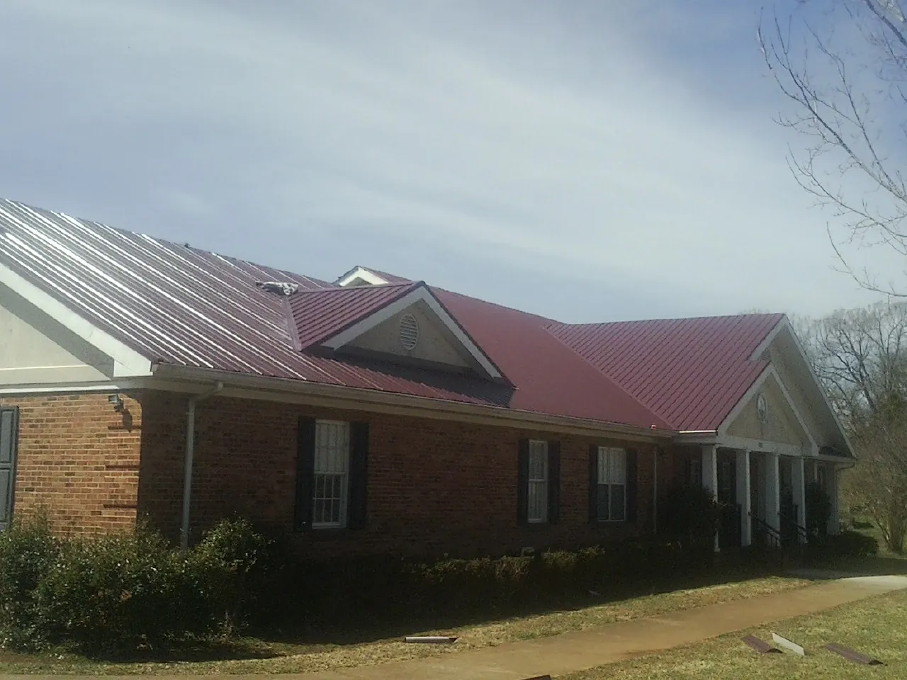 Red metal roof with gabled entries on a long brick building, from a Hail Damage Roof Repair job in New Florence