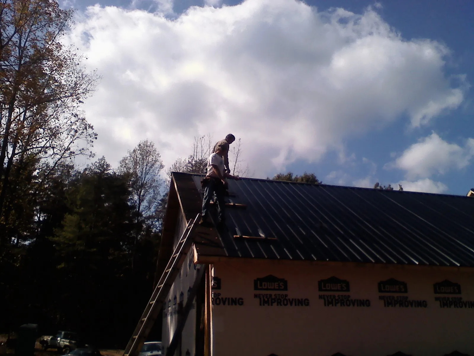 Roofer fastening dark metal panels high against a cloudy sky, from a Roof Inspection job in New Florence