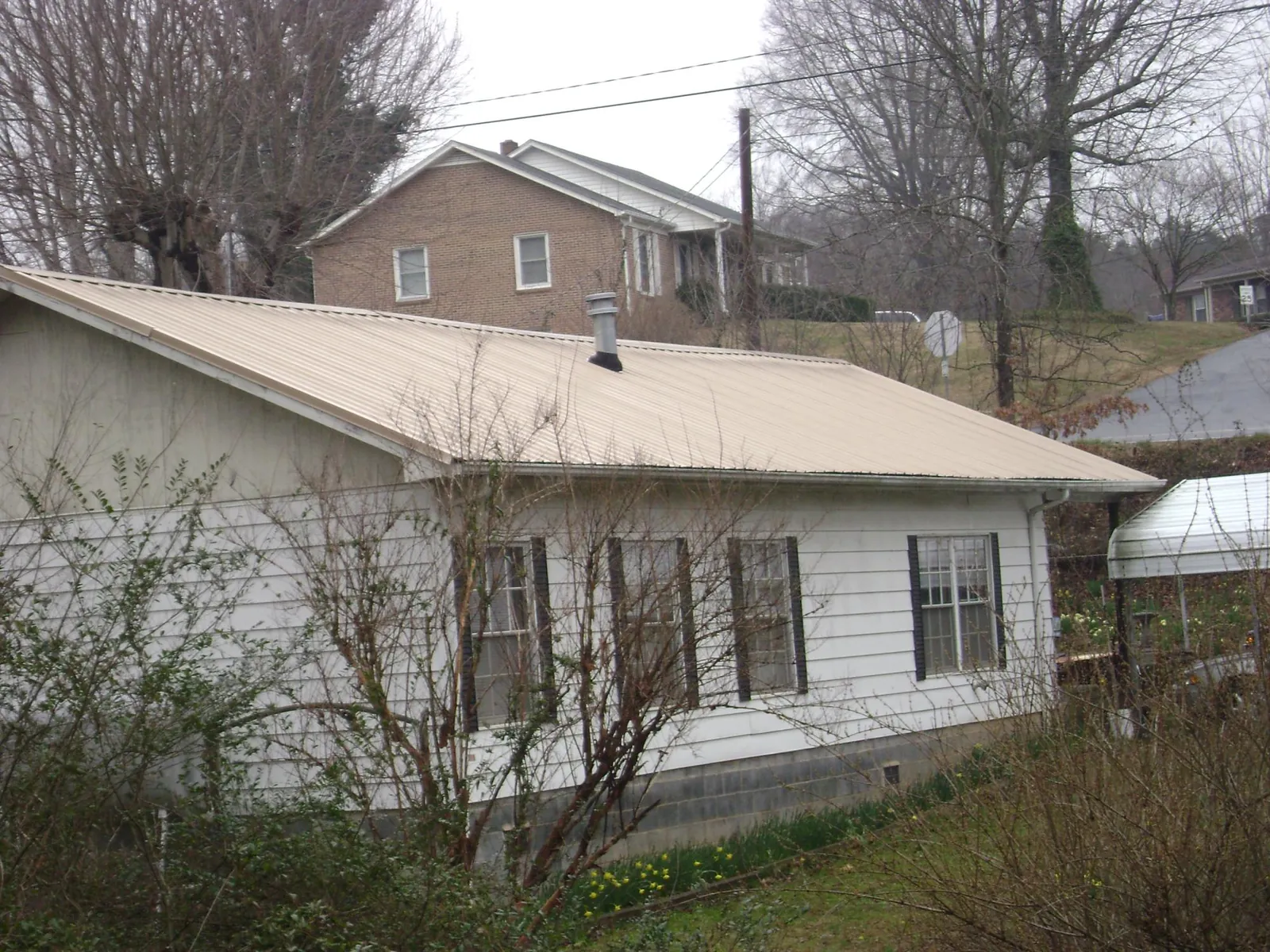 Tan metal roof on a white sided house set into a hillside — Commercial Roofing by Roofing Brothers in New Florence