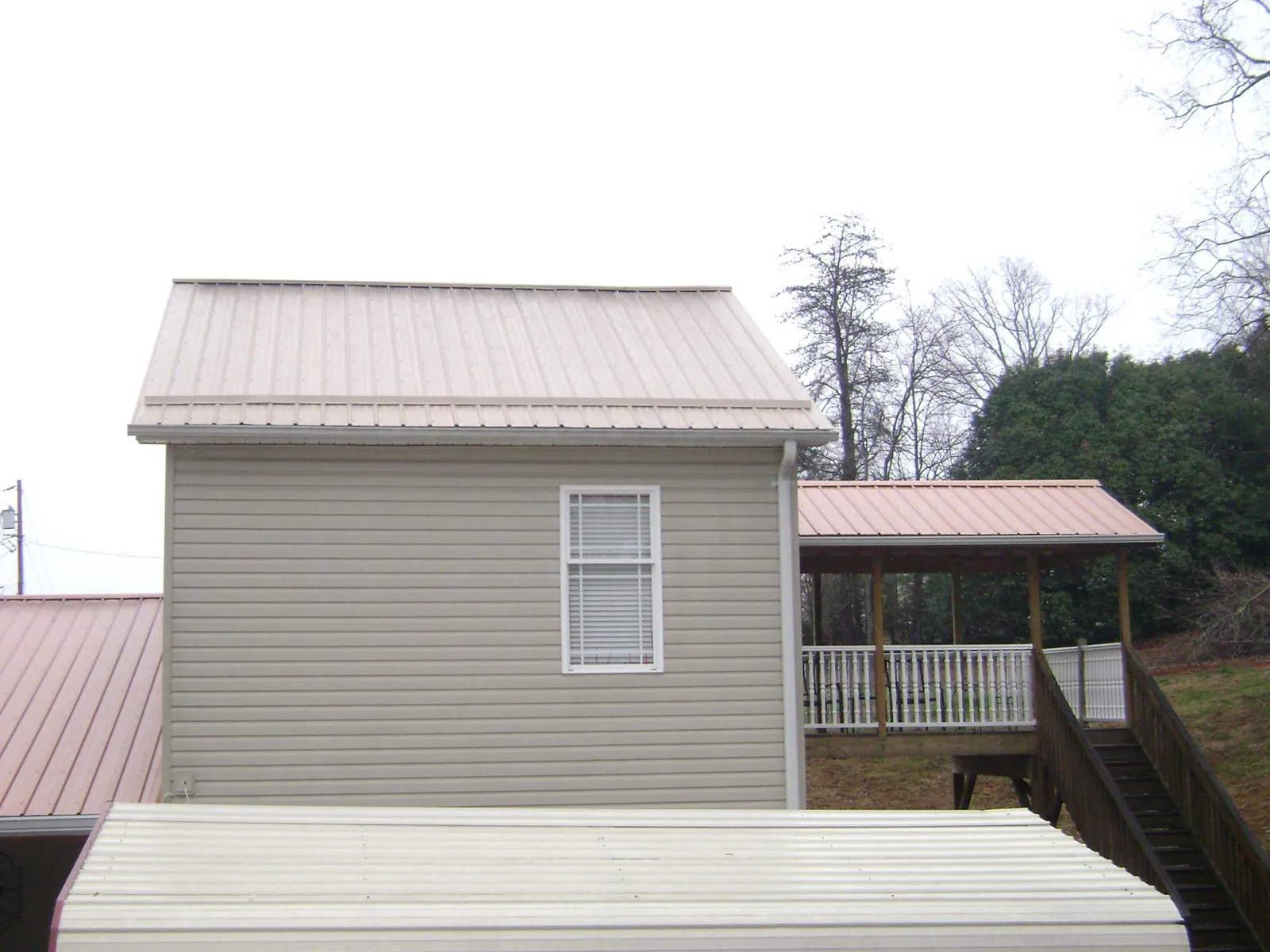 Tan metal roofs on a two story addition and attached porch, from a Roof Replacement job in New Florence